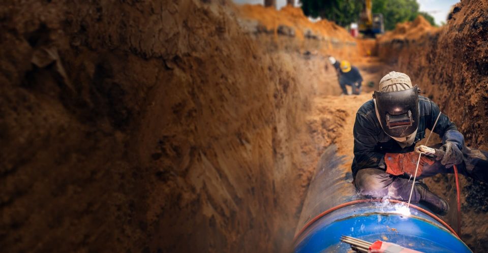 Welder welding pipeline in a deep excavation trench