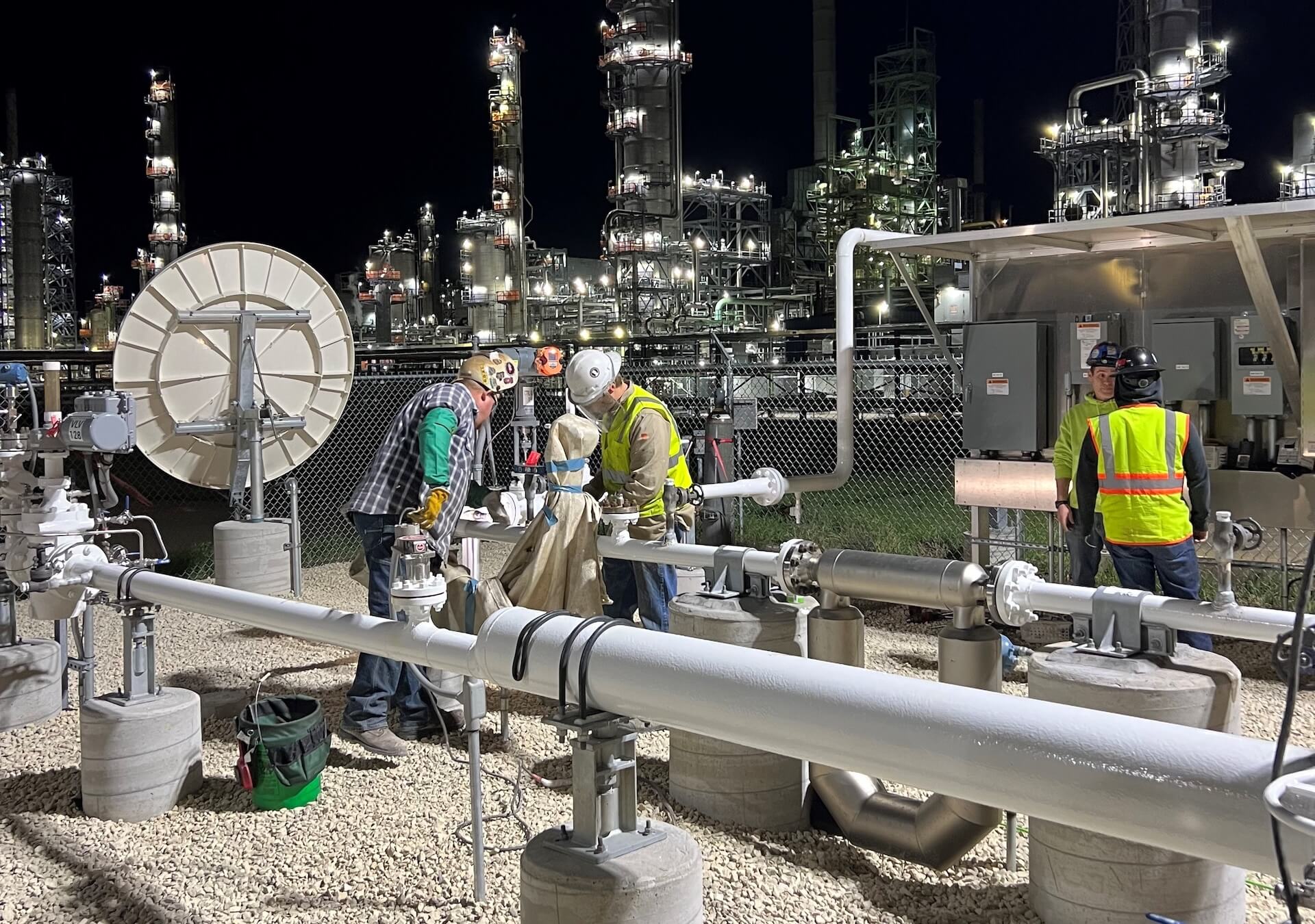 nh home team Workers in safety gear maintaining pipelines at industrial refinery night