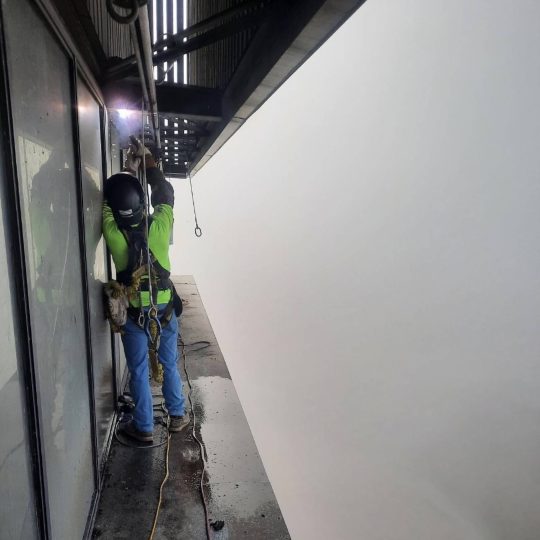Worker in safety harness welding on building exterior ledge